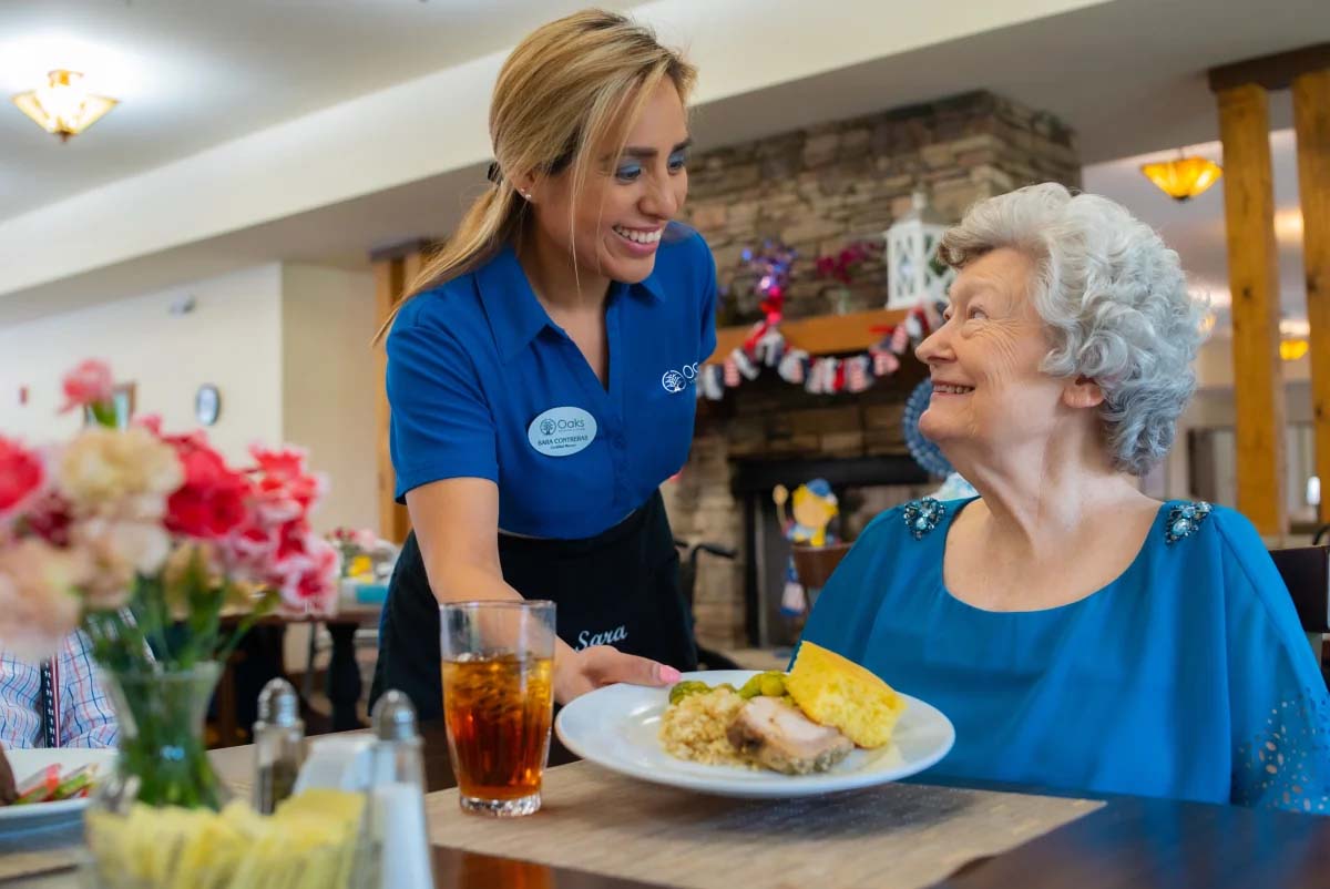 Waitress serving food to smiling elderly woman in restaurant.